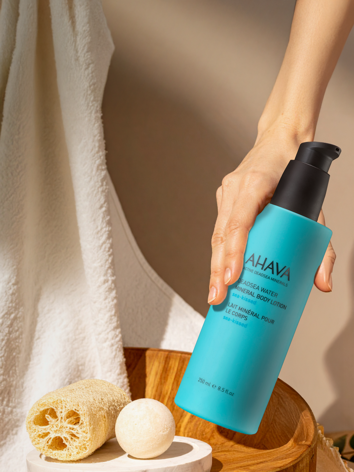 Hand holding an AHAVA Dead Sea mineral skincare bottle, illustrating the benefits of mineral-rich formulas for skin hydration, renewal, and overall skin health.